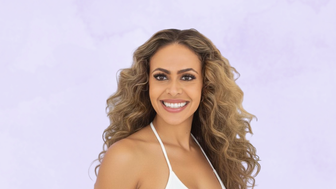 Woman smiling with long, wavy hair wearing a white top against a light purple background